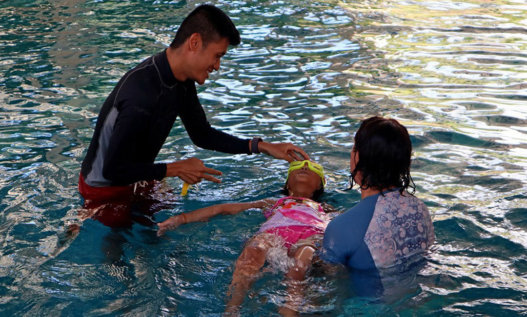 Två simlärare hjälper ett barn att flyta i en pool